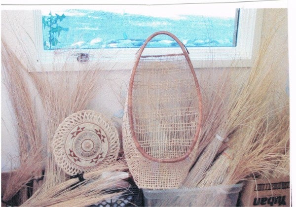 Hand woven baskets sitting amongst the reed weaving materials and set behind a white wall.
