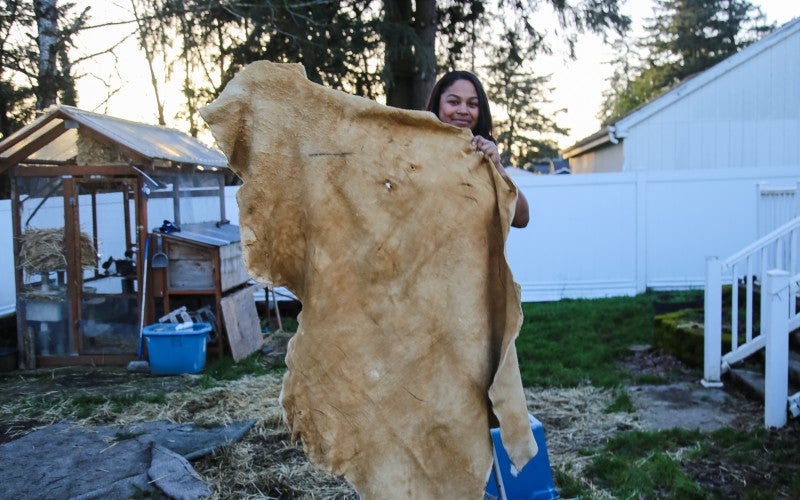 Eleeziaa stands holding a tanned hide, which is as tall as she is