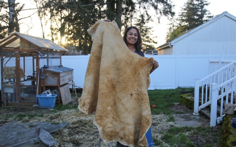 Eleeziaa stands holding a tanned hide, which is as tall as she is