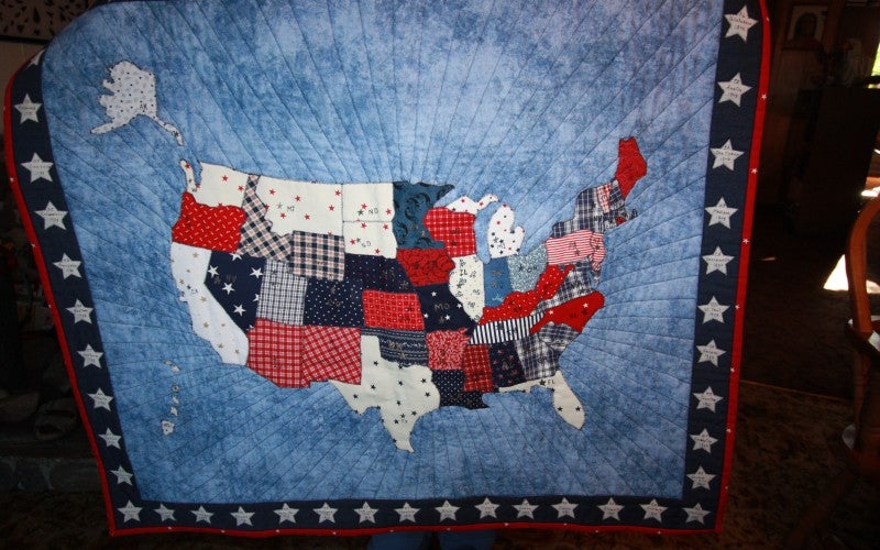 A blue quilt with a star border and a blue, red, and white map of the United States in the middle.