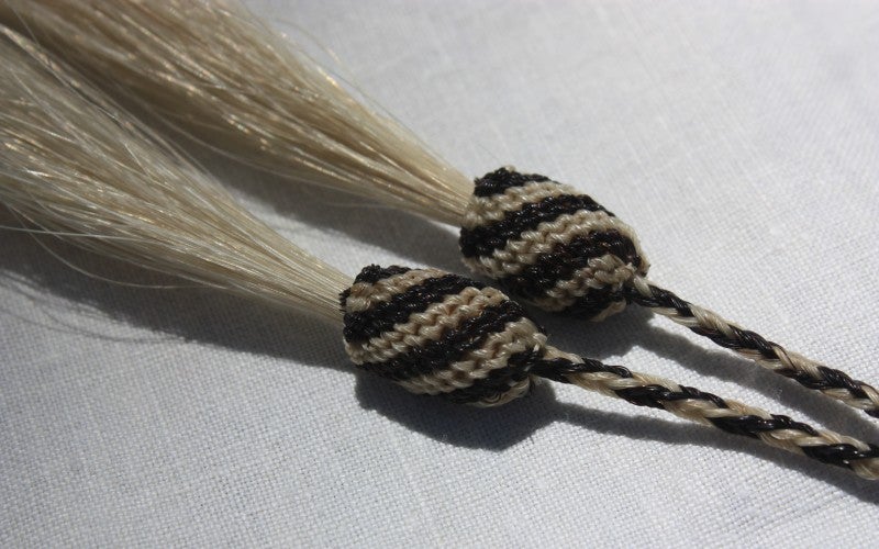 A close up image of the black and tan woven ends of a cowboy hat drawstring.
