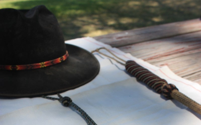 A black cowboy hat sits on top of a white table runner on top of a wooden table outside.