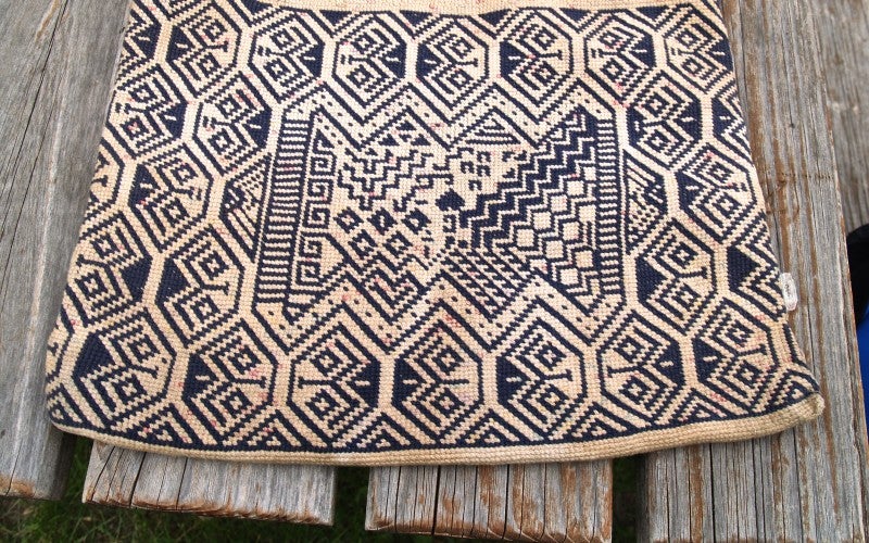 A woven bag that is tan with navy blue geometric patterns.