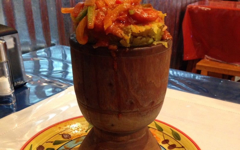 Mofongo, a dish that features mashed plantains, is served in a tall wood bowl placed on a colorful plate.