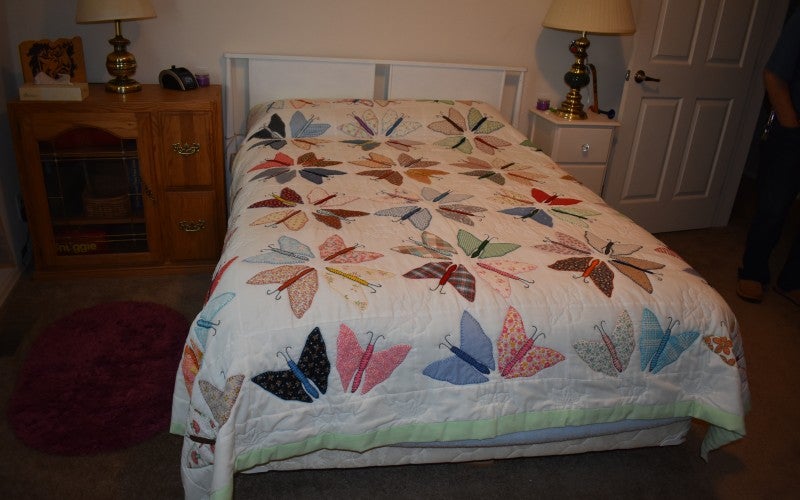 A bed made with a white quilt containing many multi-colored butterflies.