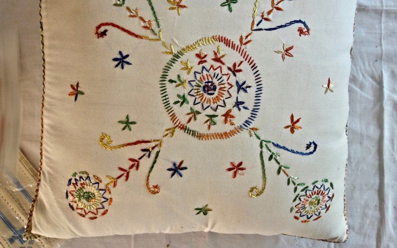 A colorfully embroidered white pillow.