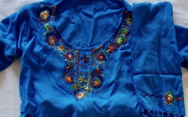 A colorfully embroidered blue shirt and scarf lay on a white sheet.
