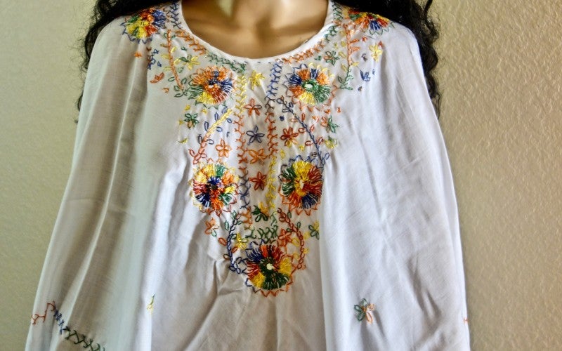 A colorfully embroidered white shirt is displayed on a mannequin. 