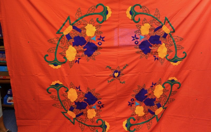 A bright orange sheet with blue, yellow, and green abstract flower embroidery.