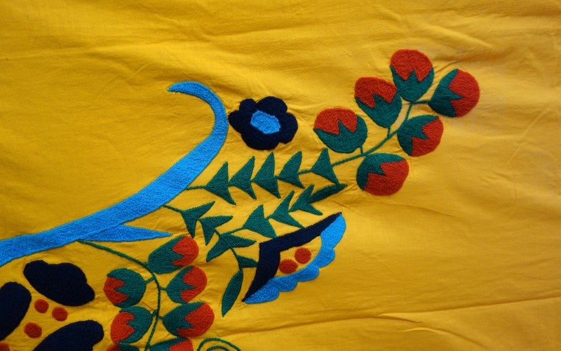 A yellow sheet embroidered with red, green, blue, and black plants.