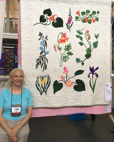 Lisa posing next her white quilt with detailed quilted flower designs.