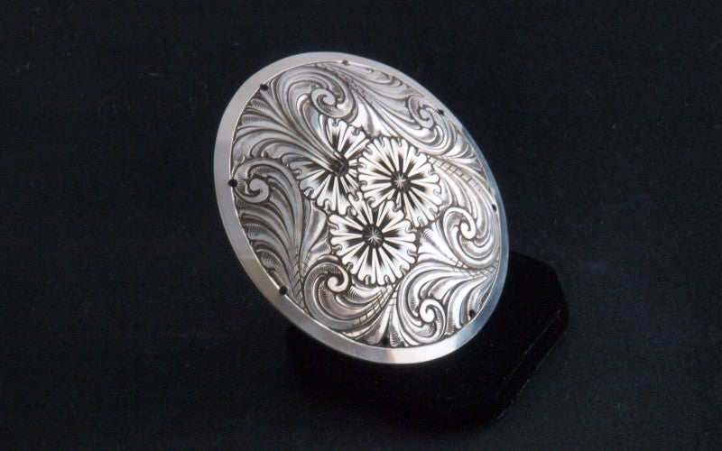 A round piece of engraved silver with abstract floral designs