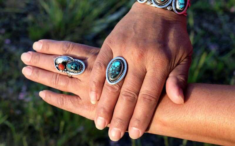 A person modeling two rings. Both rings are silver with turquoise stones. 