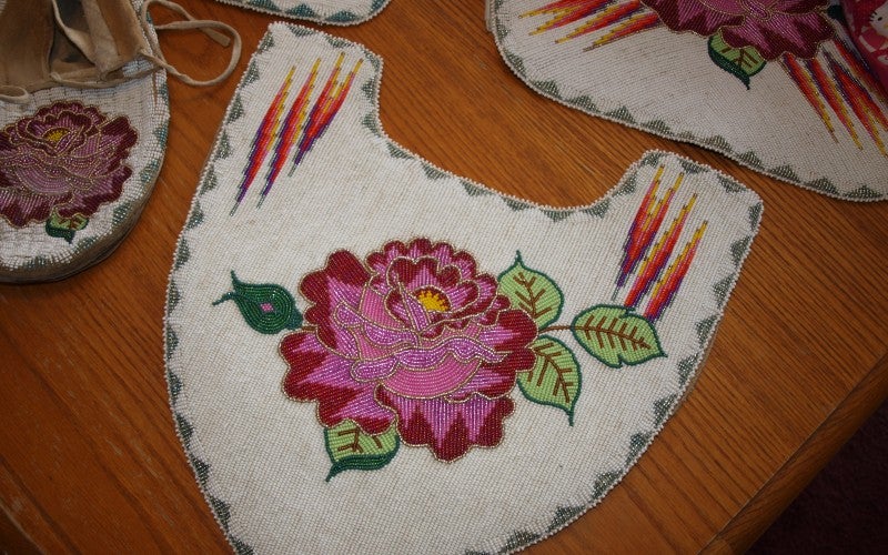 A white piece of regalia with a pink rose in the middle.