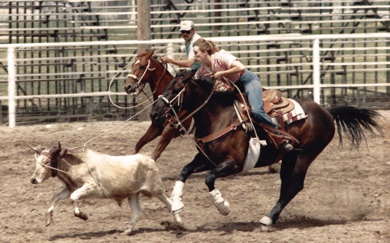 A man and a woman ride brown horses and rope a small white cow.