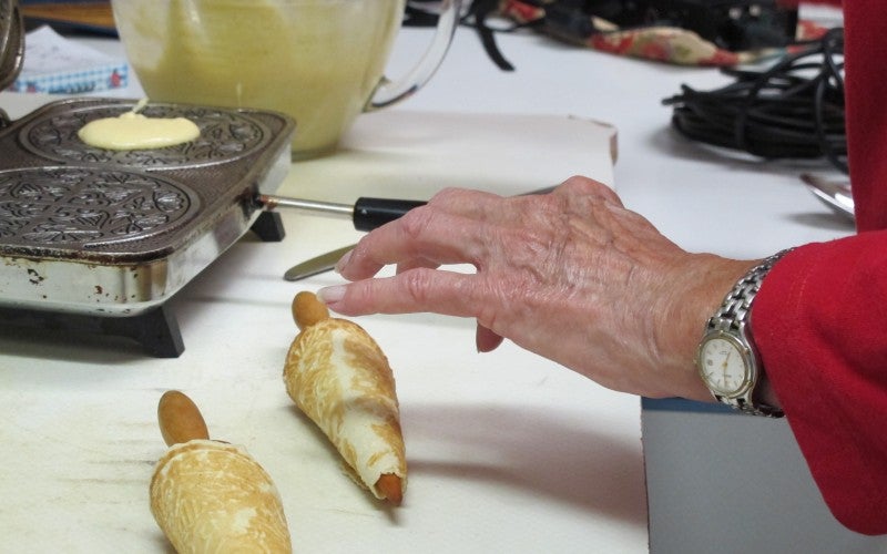 Two piece of lefse sit in front of an iron where dough is being cooked.