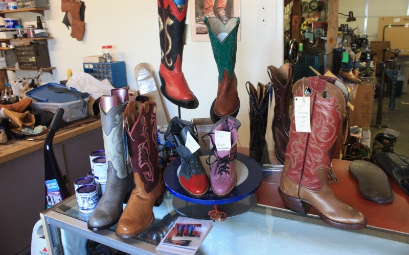 Cowboy boots of various colors and sizes are displayed on a glass counter.