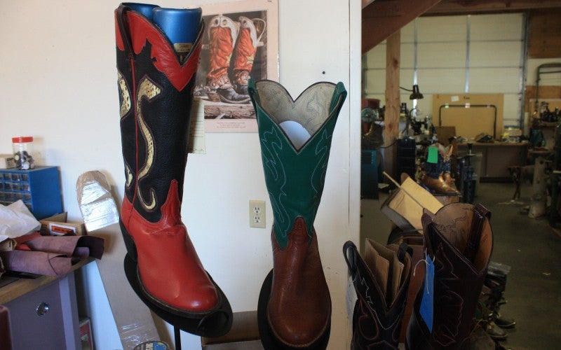 Two displayed cowboy boots. One boot is red and black and the other boot is red and green.