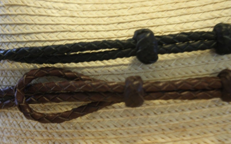 A close up image of brown and black woven strings on a tan cowboy hat.