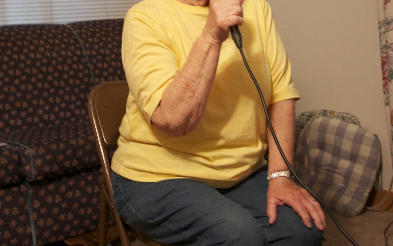 A woman wears a yellow shirt and sings into a microphone.
