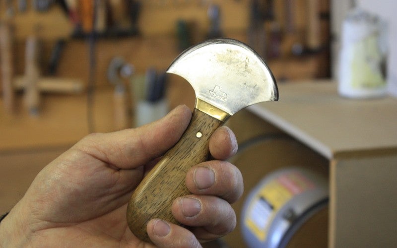 A hand holds a sharp metal tool with a wooden handle.