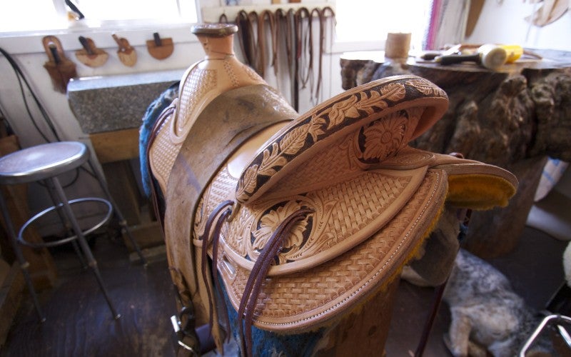 Intricately carved western saddle with leather tassles, a high back seet, and a horn at the front for the rider to hold onto.