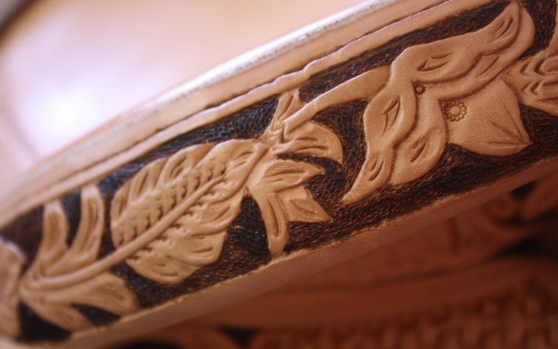 Close-up of decorative carving of flowers along the edge of the high back seat of the saddle.