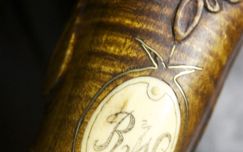 Close-up of a wood handle with an inset metal plate etched with the letters R W.