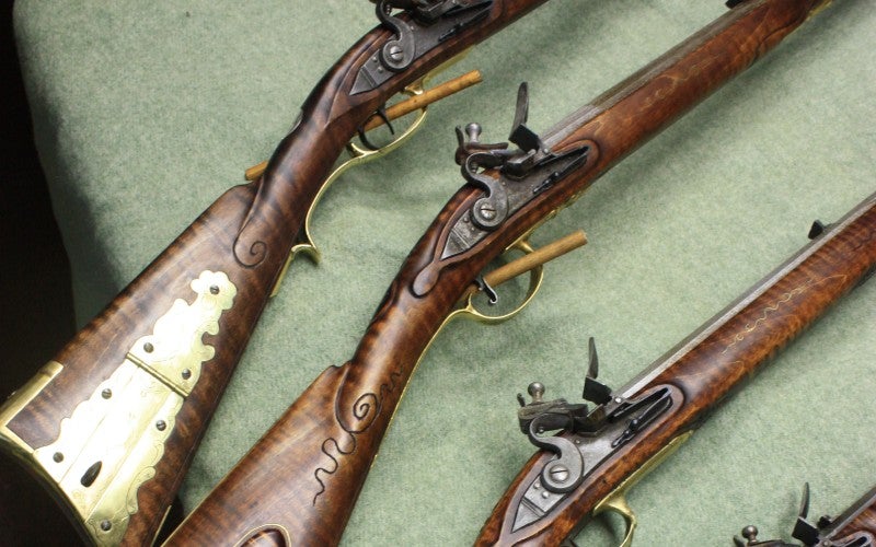 Three wood rifles laid out on a green table cloth next to a revolver.
