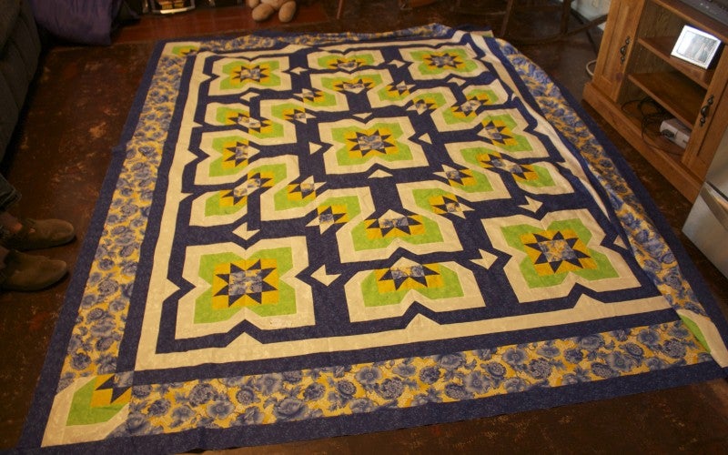 A blue, gree, white, and yellow quilt with flower designs.