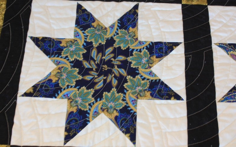 A white quilt with an eight point star with a floral design inside.