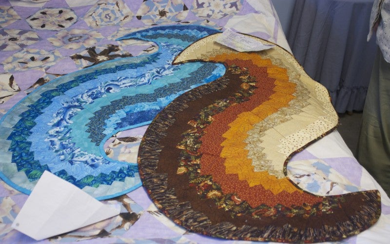 A blue quilt and a brown and red quilt shaped like waves.