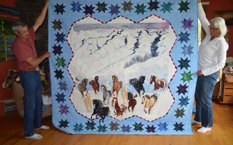 A quilt depicting wild horses running down snow-covered mountains.
