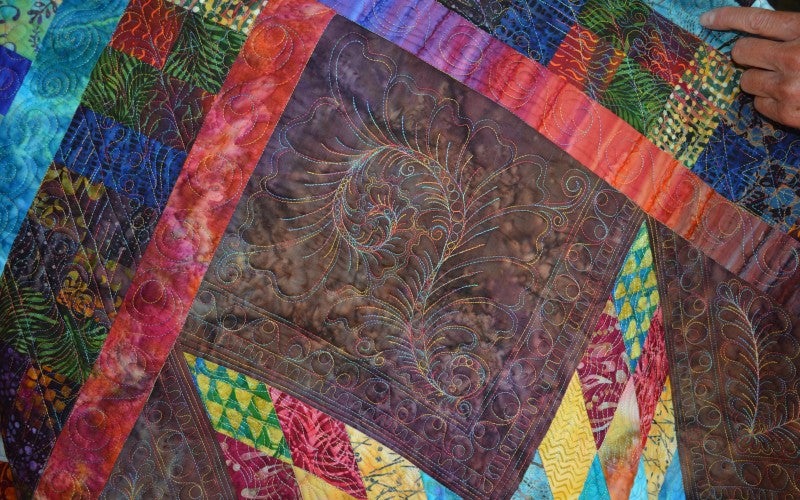 A multicolored quilt square with swirly embroidery.