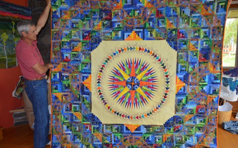 A multicolored blue, green, and orange quilt with a compass in a beige square in the middle.