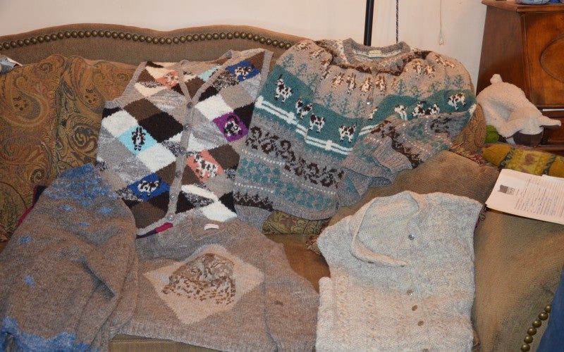 Several knitted sweaters on a brown loveseat