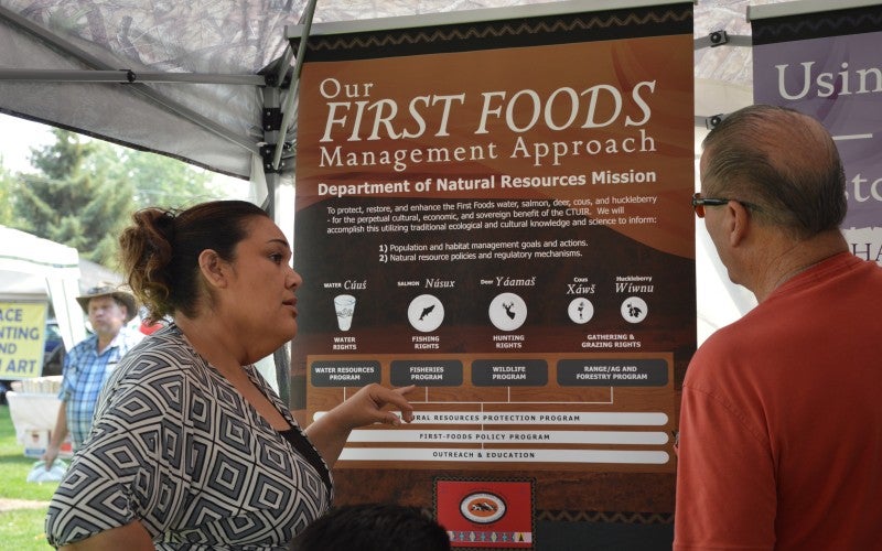 Red Elk talks to someone in front of an informational poster about first foods
