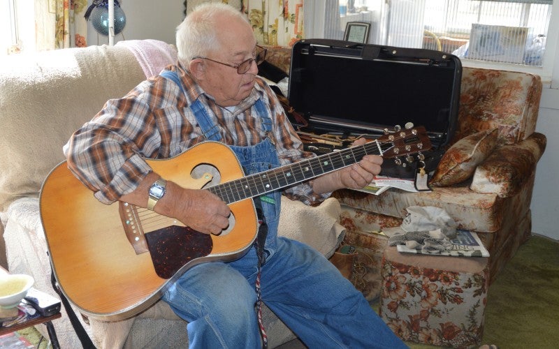 Robert plays acoustic guitar in an armchair