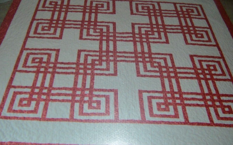 A white quilt containing red geometric patterns.
