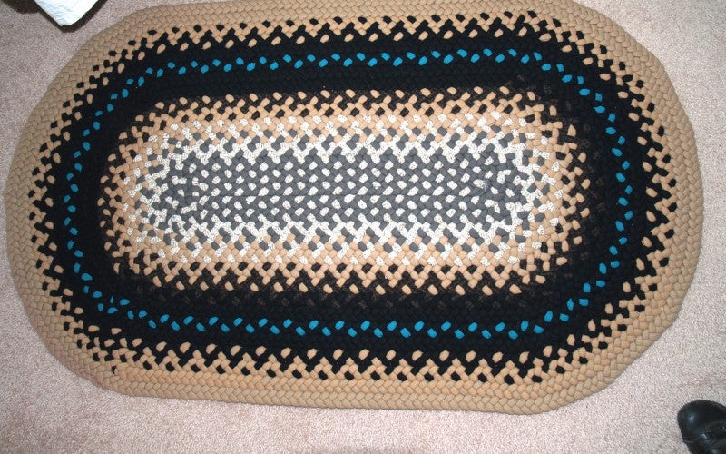 A white, tan, black, and blue oval-shaped braided rug.