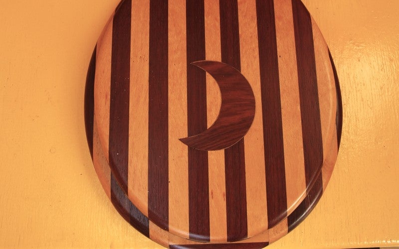 A striped wooden toilet seat with a crescent moon in the center