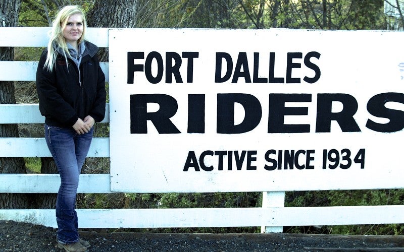Howell stands next to a white sign that says "Fort Dalles Riders active since 1934" 