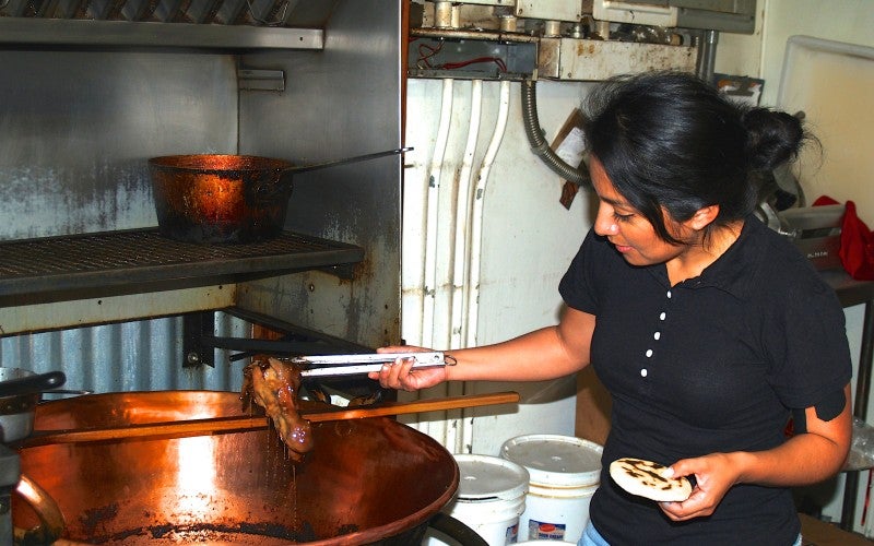 A woman holds a chunk of meat with tongs over a large copper pot.