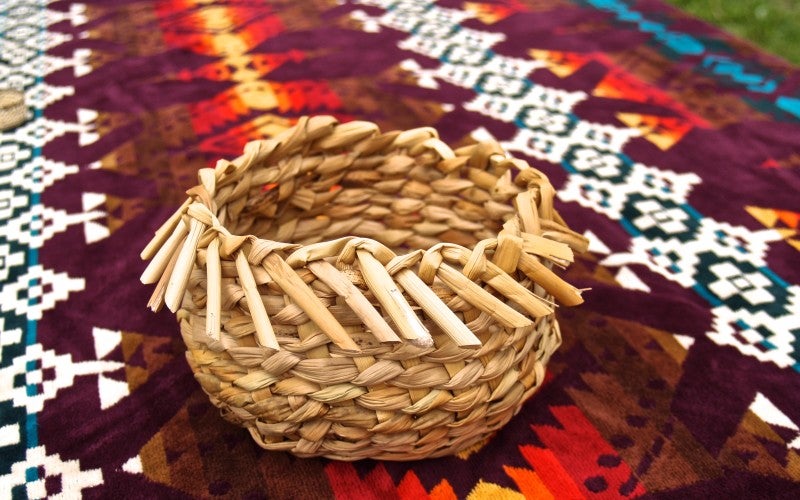 A circular basket sitting on a blanket with brown, red, and yellow geometric patterns.