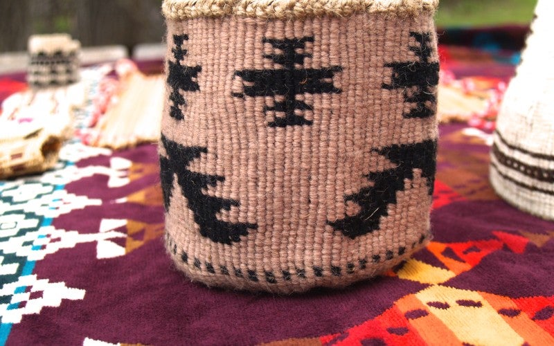 A cylinder shaped tan basket with black geometric designs woven into it.