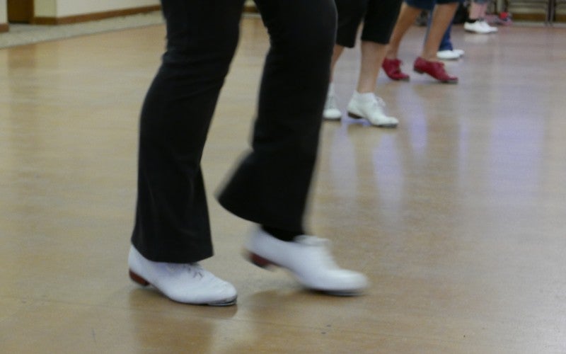 A close up image of someone dancing in white clog shoes.