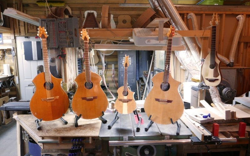 Four acoustic guitars rest on stands atop a large workbench