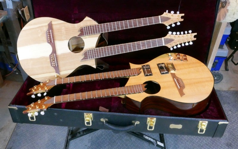 Two double neck guitars rest on a black rectangular instrument case with a red velvet interior