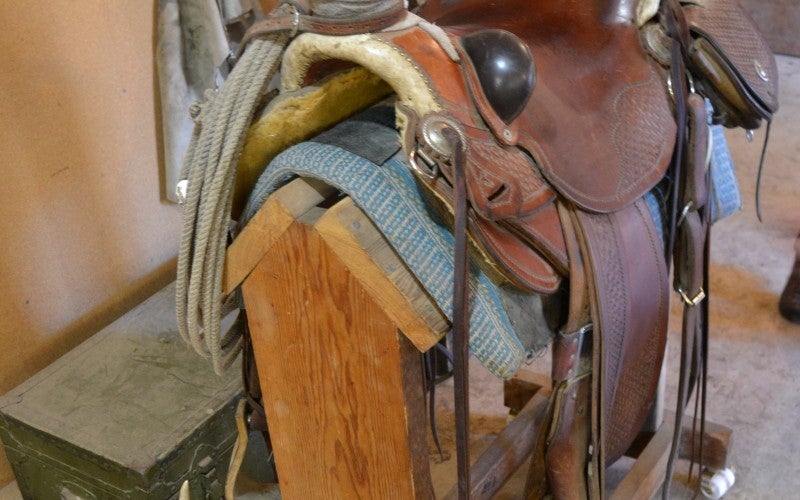 A western leather horse saddle with a high back and front sits on a wood stand.