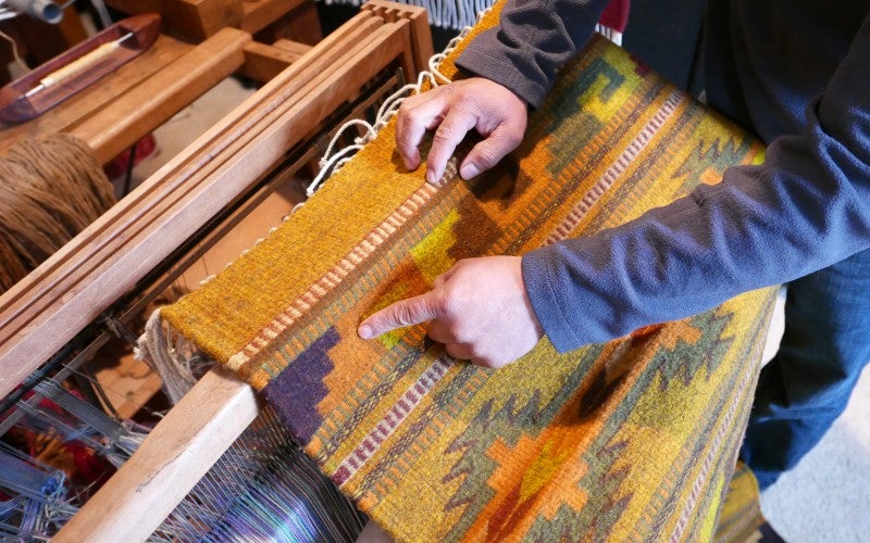A yellow, green, orange, and blue rug on a weaving machine.